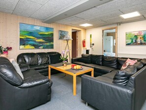 A room with two black leather sofas, a wooden coffee table with fruit, and paintings on the walls. - 24 Person Holiday Home in Lokken (Lokken)