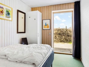 A bedroom with a bed, a wardrobe, a window with a view of a field, and a painting on the wall.