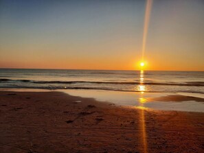A beach with a sunset, waves, and a clear sky.