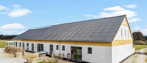 A single-story building with a sloped roof, large windows, and a small garden area in front.