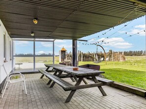 An outdoor covered patio with picnic tables, a hanging chair, and a view of the countryside.