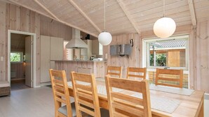 A wooden interior with a dining area featuring a wooden table and chairs, a kitchen with modern appliances, and a large window providing natural light. - 8 Person Holiday Home in Idestrup-by Traum (Idestrup)