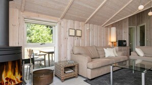 A cozy living room with a fireplace, a sofa, a glass coffee table, and a wicker side table. - 8 Person Holiday Home in Idestrup-by Traum (Idestrup)