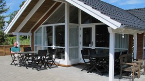 A covered outdoor seating area with a table and chairs, large windows, and a wooden deck. - 8 Person Holiday Home in Idestrup-by Traum (Idestrup)