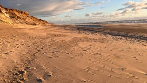 A sandy beach with footprints and a dune on the left. - 5 Person Holiday Home in Ringkobing (Ringkobing)