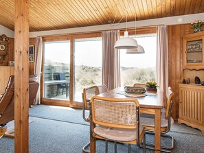 A wooden interior with a dining table, chairs, and a view through large windows. - 5 Person Holiday Home in Ringkobing (Ringkobing)