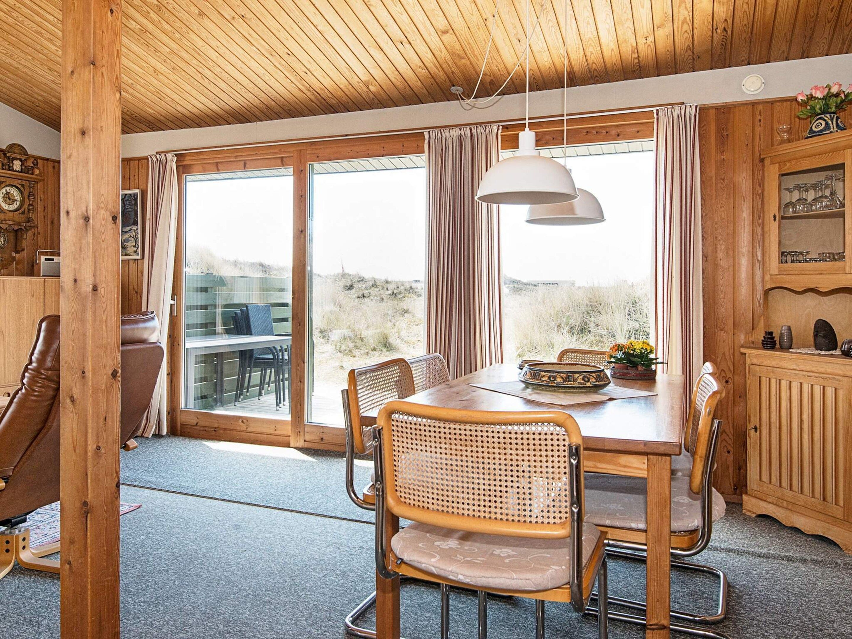 A wooden interior with a dining table, chairs, and a large window.