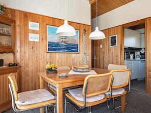 Une salle à manger aux murs lambrés, avec une table en bois, des chaises en osier et deux lampes suspendues.