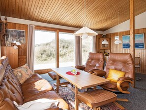 Une pièce chaleureuse avec un plafond en bois, des meubles en cuir et de grandes fenêtres donnant sur l’extérieur.
