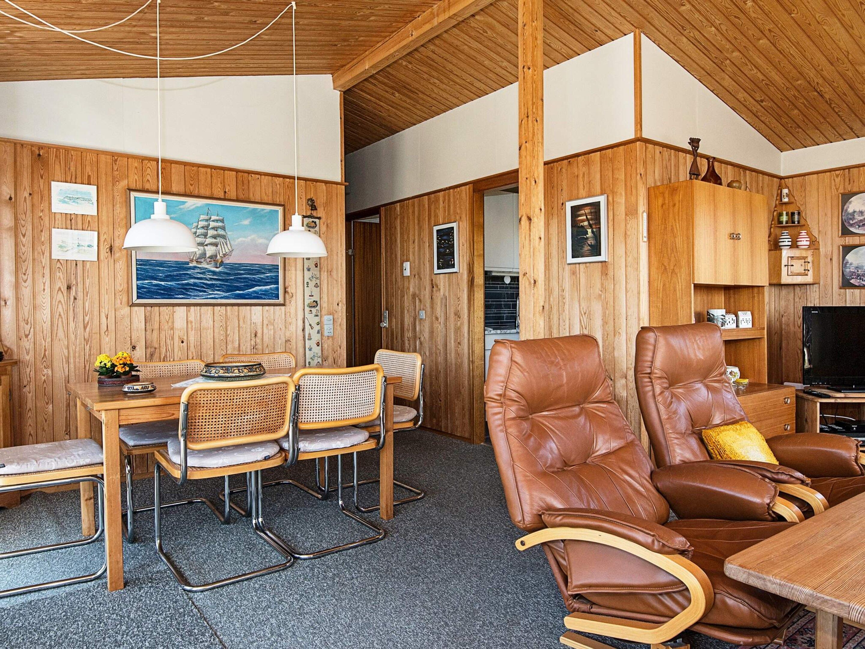 Une pièce aux murs en bois, avec une table à manger et des chaises, un canapé et un téléviseur.