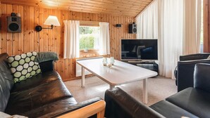 Un salon chaleureux avec des murs en bois, un canapé en cuir, une table basse blanche et un téléviseur.