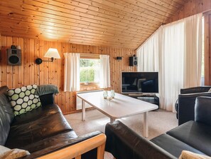 Un salon chaleureux avec des murs en bois, un canapé en cuir, une table basse blanche et un téléviseur.
