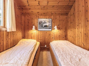 Une chambre rustique en bois avec deux lits, un tableau encadré représentant un cheval et deux lampes fixées au mur.