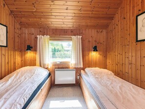 Una habitación con dos camas individuales, una ventana con cortinas, un radiador y dos lámparas de pared.