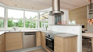 A modern kitchen with wooden cabinets, a stainless steel range hood, and a large window providing a view of greenery. - Luxury Spa Retreat by Beach - By Traum Ferienwohnungen (Glesborg)