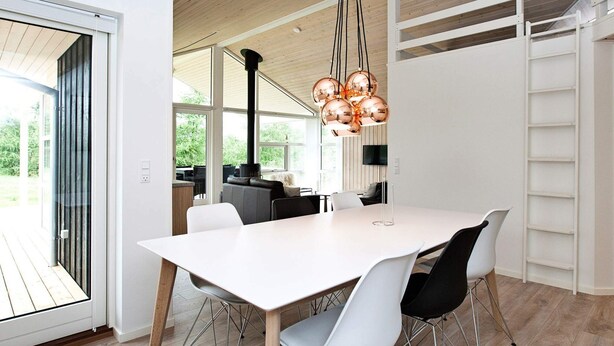 A modern dining area with a white table and chairs, a large window, and a hanging copper chandelier. - Luxury Spa Retreat by Beach - By Traum Ferienwohnungen (Glesborg)