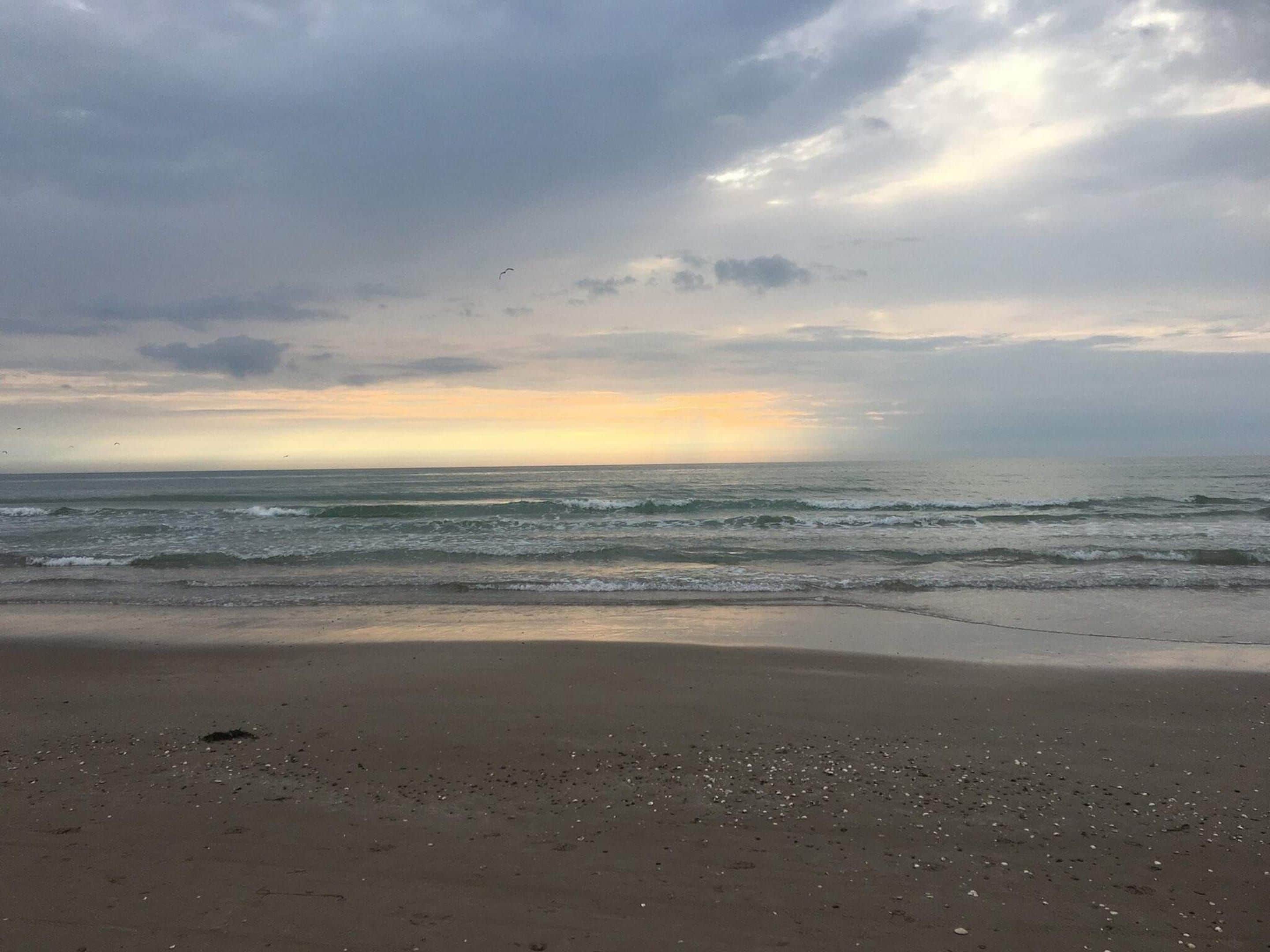 A beach with waves, a cloudy sky, and a sunset.