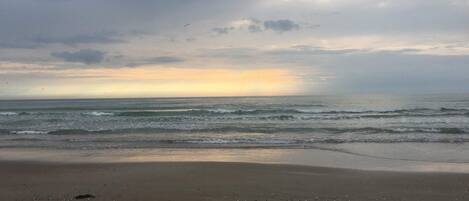 A beach with waves, a cloudy sky, and a sunset.
