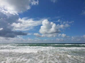 Een strand met golven en een gedeeltelijk bewolkte lucht.