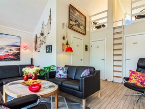 A modern living room with a black leather sofa, a round coffee table with decorative items, a painting, and a ladder leading to an upper level.