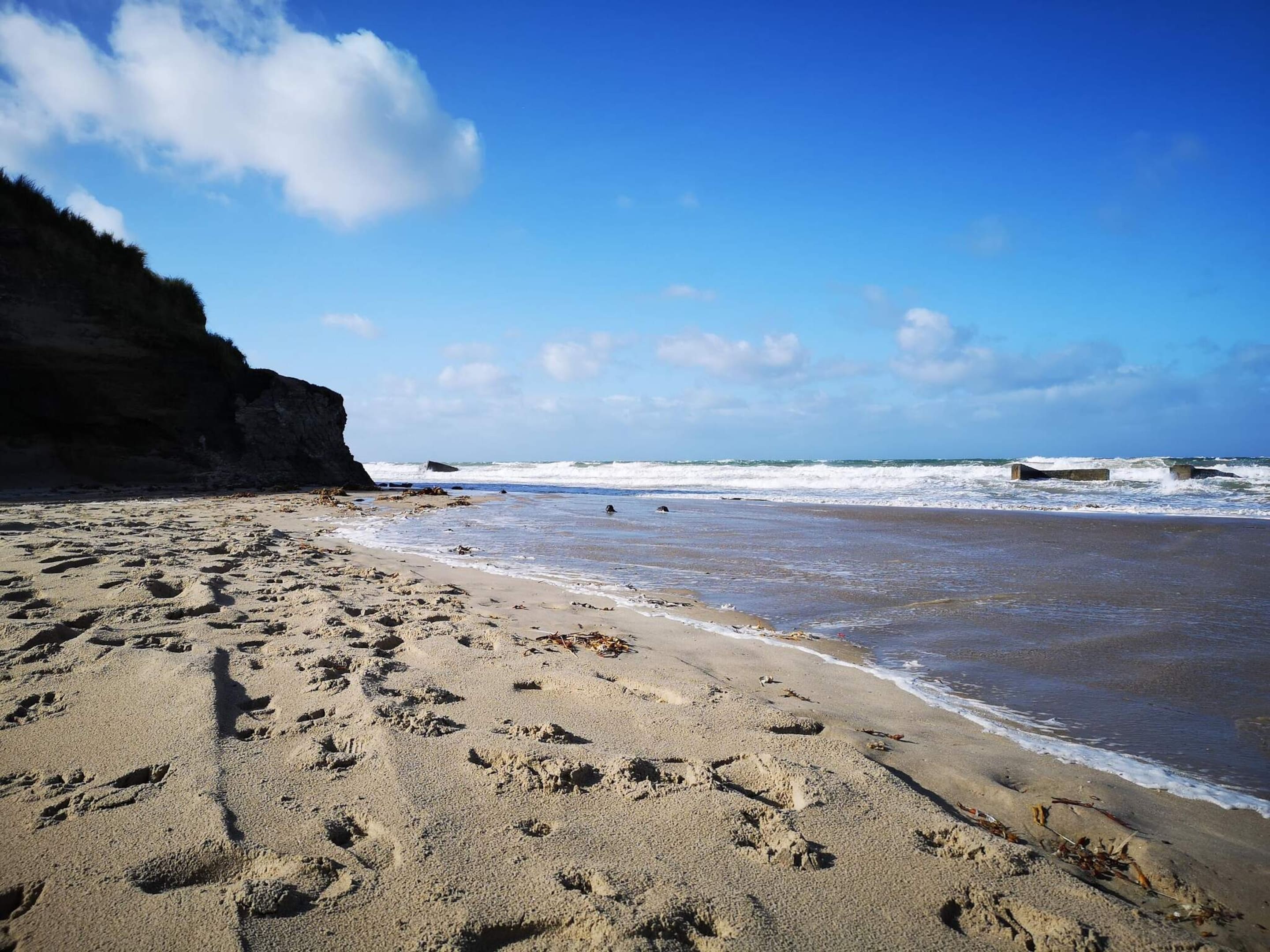 A beach with footprints, waves, and a cliff.