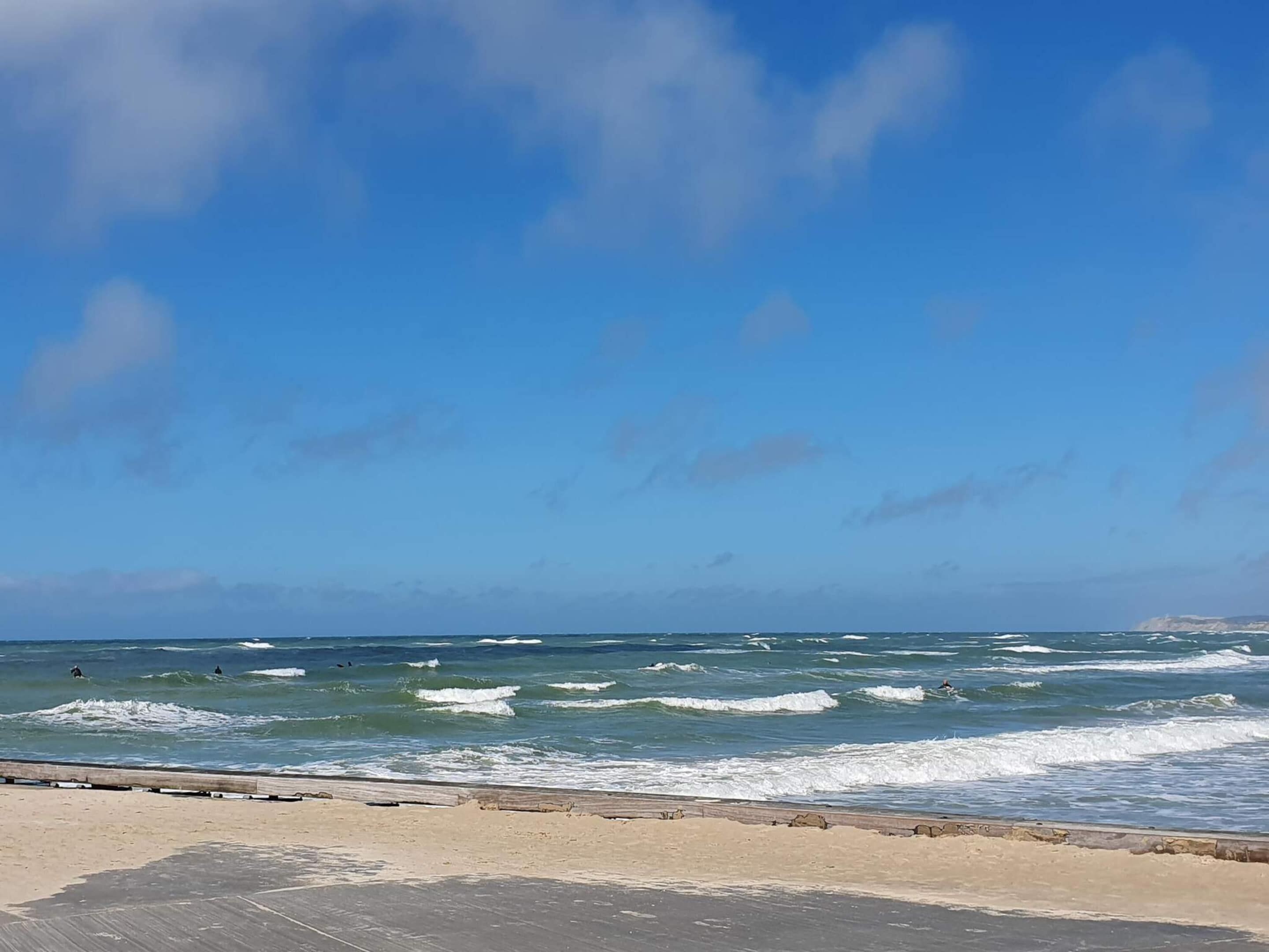 A beach with waves, a clear sky, and a wooden boardwalk.
