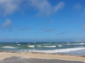 Une plage avec des vagues, un ciel dégagé et une promenade en bois.