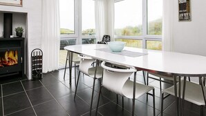 Une cuisine moderne avec une table blanche, des chaises noires, une cheminée et de grandes fenêtres.