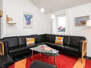 Un salon moderne avec un canapé en cuir noir, une table basse en verre et un tapis rouge.