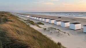 Une rangée de cabanes de plage blanches s’étend le long d’une plage de sable, offrant une vue sur l’océan.