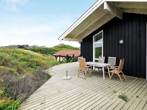 A wooden deck with a table and chairs, overlooking a grassy area with a building in the background.