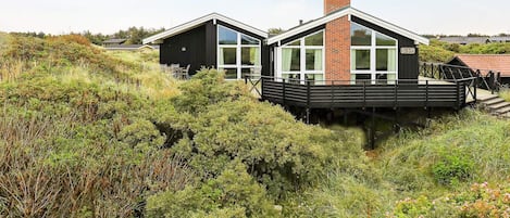 A modern two-story building with a deck, surrounded by dense vegetation.
