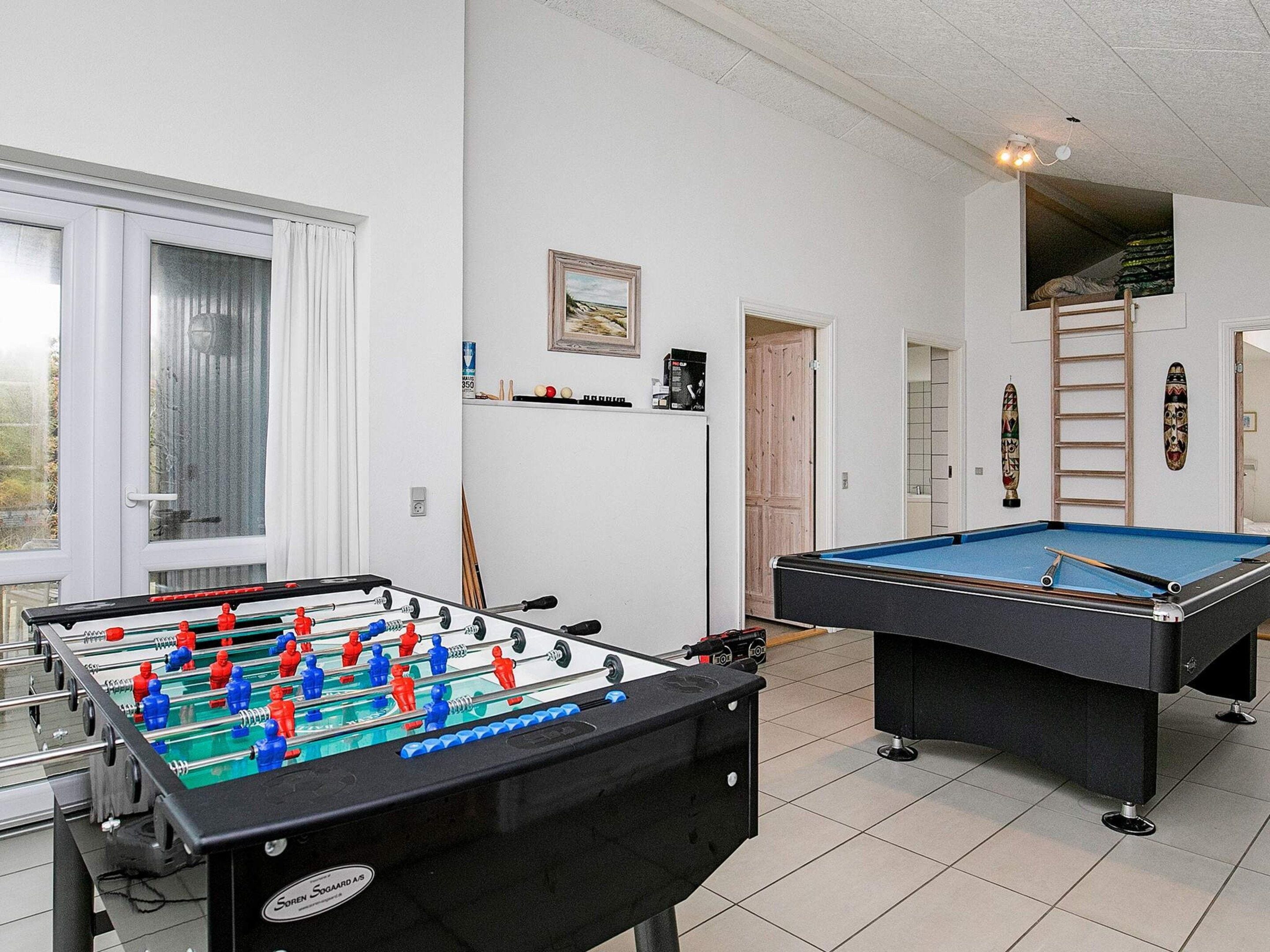 A room with a foosball table, a pool table, and a window with curtains.