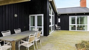 Une terrasse avec une table et des chaises, un bâtiment noir aux fenêtres à cadre blanc et une cheminée en briques.