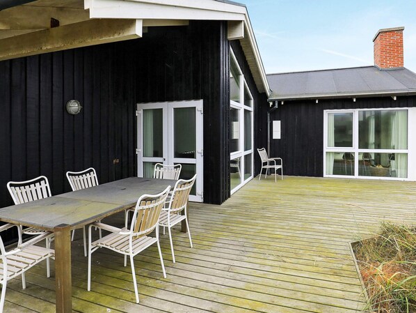 Une terrasse avec une table et des chaises, un bâtiment noir aux fenêtres à cadre blanc et une cheminée en briques.