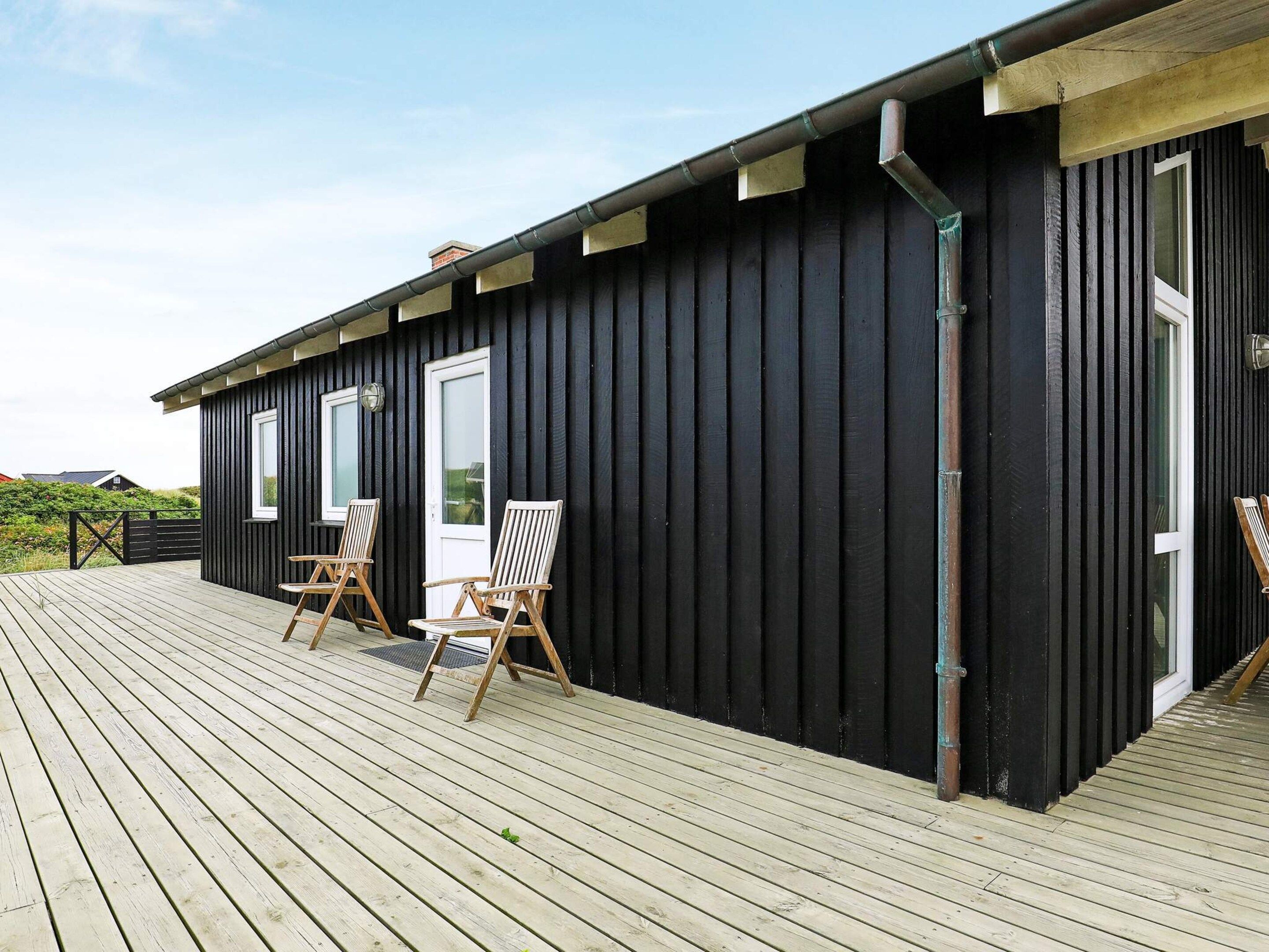 A wooden deck with two wooden chairs and a door to a building.