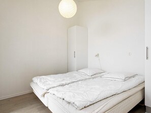 A minimalist bedroom with a bed, a wardrobe, and a pendant light. - 4 Star Holiday Home in Lokken (Lokken)
