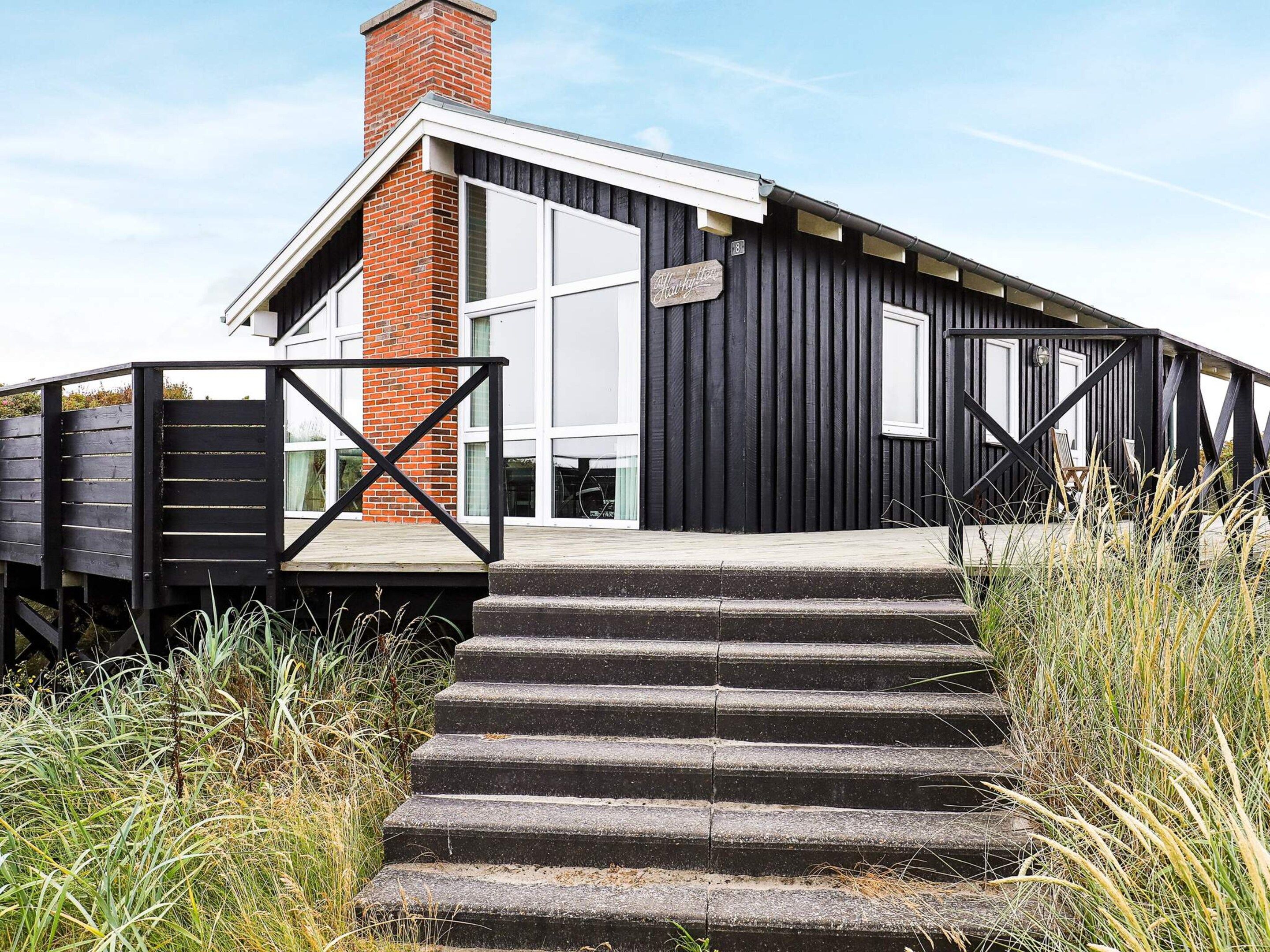 A modern building with a black exterior, a brick chimney, and a wooden deck.