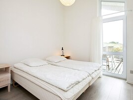 Un dormitorio minimalista con una cama grande, una mesita de noche con lámpara y vistas a través de un ventanal corredero.