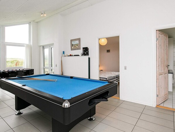 A pool table in a room with a window, a door leading to another room, and a small shelf with items.