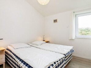A bedroom with a bed, bedside table, lamp, and a window with a view.