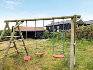 A wooden swing set with two swings and a ladder, set against a backdrop of a building with a red roof. - 4 Star Holiday Home in Lokken (Lokken)