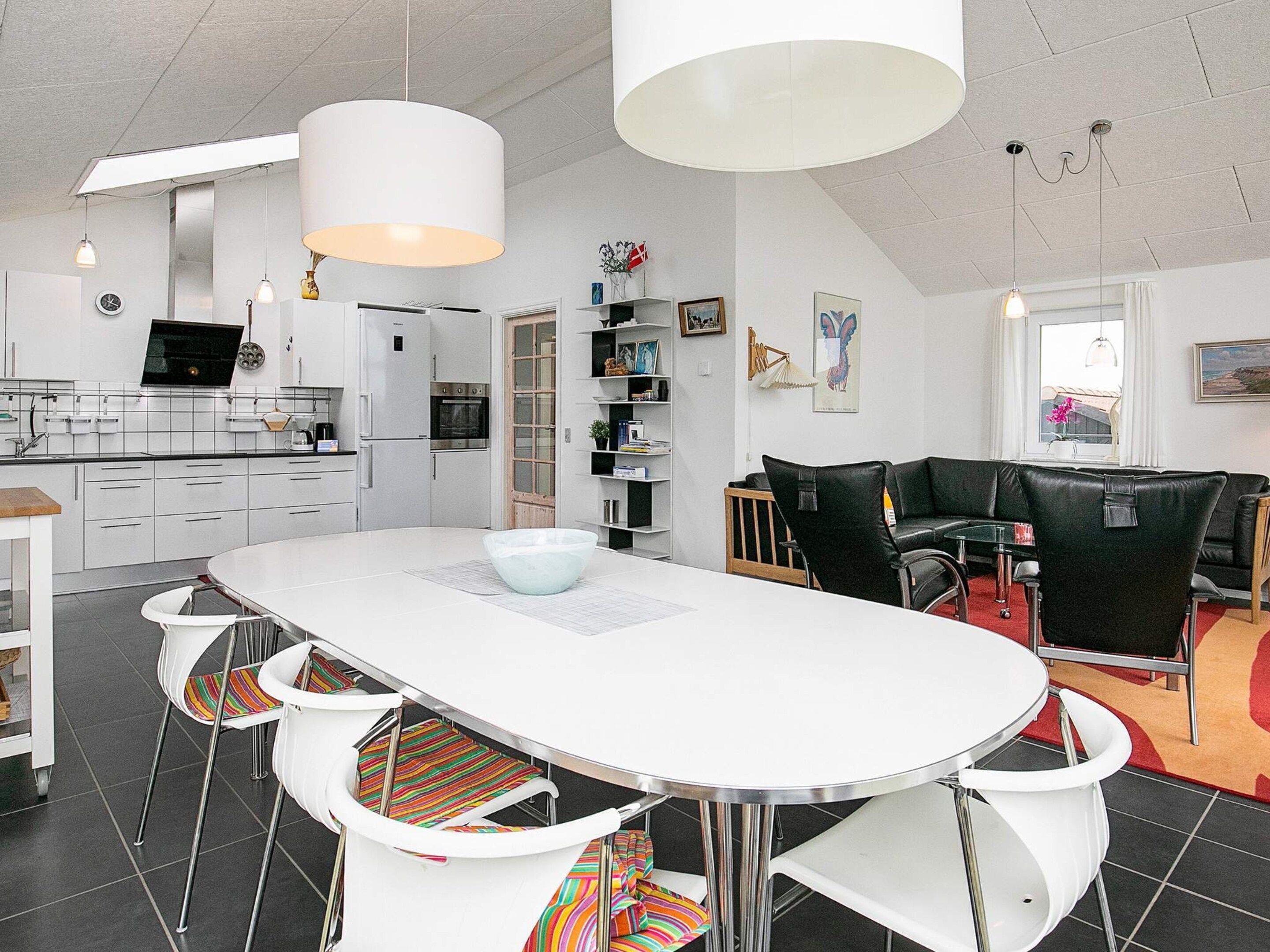 Une cuisine moderne avec des meubles blancs, un coin repas doté d’une table et de chaises blanches, et un canapé en cuir noir.