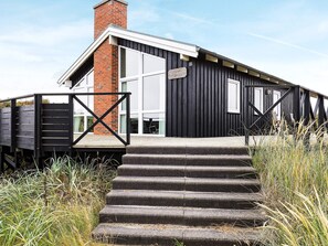 A modern building with a black exterior, a brick chimney, and a set of concrete steps leading to a wooden deck.