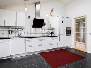Una cocina moderna con armarios blancos, encimera negra, alfombra roja, horno empotrado y un ventanal grande.