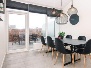 A modern dining area with a glass door leading to an outdoor patio, featuring a black table, black chairs, and pendant lighting. - 5 Star Holiday Home in Ringkobing (Ringkobing)