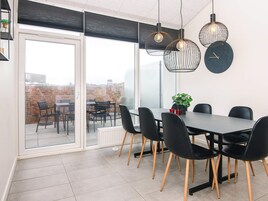 Un'area pranzo moderna con una porta vetrata che dà su un patio esterno, con un tavolo nero, sedie nere e illuminazione a sospensione.