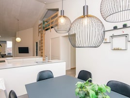 Uma cozinha moderna com ilha central, luminárias pendentes e escada que dá acesso a um andar superior.