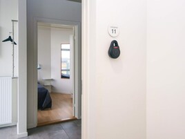 Un corridoio con una porta che dà su una camera da letto. Si vede un attaccapanni con grucce, un organizer per scarpe a parete e una finestra con vista all'esterno.