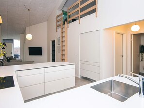 A modern kitchen with a built-in sink, white cabinetry, and a wooden ladder leading to an upper level.